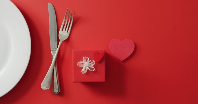 Plate and cutlery with gift on red background at valentine's day