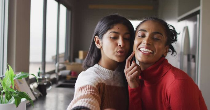 Video of happy biracial female friends kissing on cheek