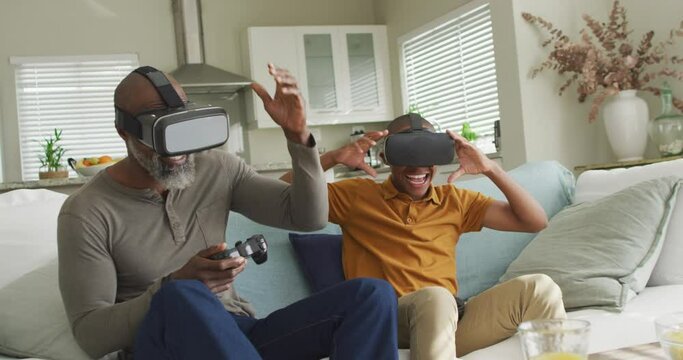 Video of happy african american father and son wearing vr headsets and playing video games
