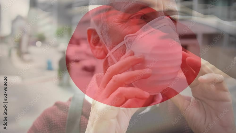 Wall mural Animation of flag of japan waving over caucasian man wearing face mask in city street