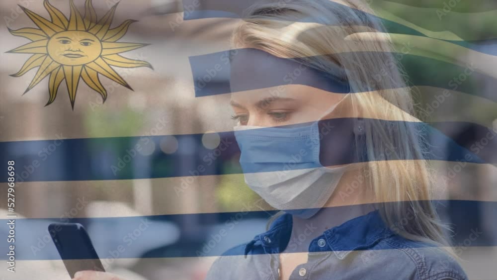 Wall mural Animation of flag of uruguay waving over caucasian woman wearing face mask in city street