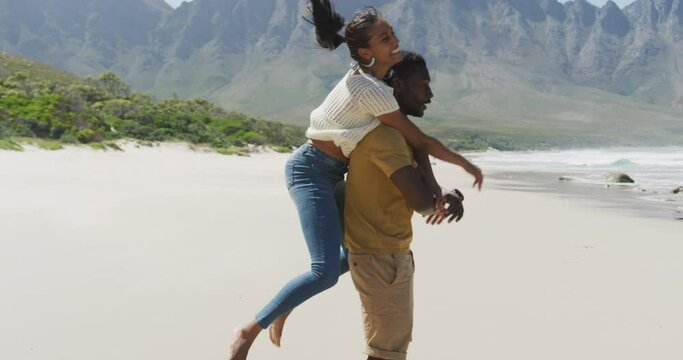 African american man giving piggyback ride to his wife at the beach