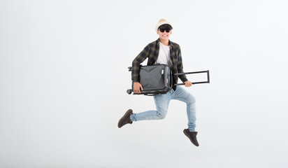 Jumping portrait of young happy wearing black glasses smiling handsome Asian tourist man with baggage ready to travel isolated on white studio background