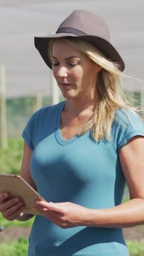 Video of caucasian woman with tablet standing in greenhouse
