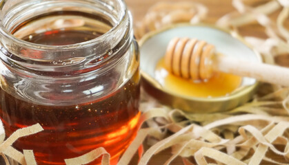 Honey in glass jar with blurred honey dipper in background. Health and beauty product sustainable lifestyle concept.