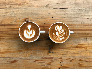 tulip and rosetta pattern latte art of two cups of hot latte coffee put in the middle of natural brown and beautiful pattern wood table