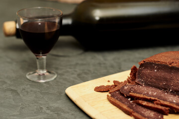 sliced basturma on a plate next to a bottle of wine and a glass