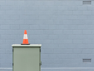 A single orange traffic cone in front of a grey-blue brick wall
