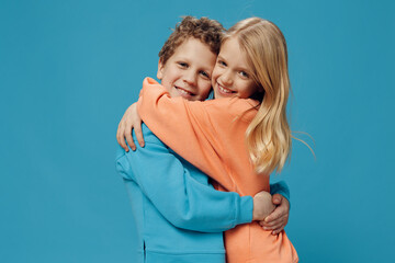 beautiful, cute children, brother and sister stand on a blue background hugging each other. Themes of relationships and friendship between children