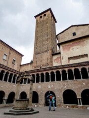 Unrecognizable tourist family with a man pointing to bell tower in Basilica Santuario Santo Stefano with Il Chiostro well courtyard © mino21