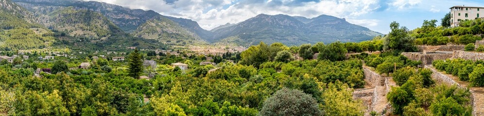 Fototapeta na wymiar Wide panorama over the lush valley of Soller from Mallorca hiking trail GR-221 Camí de Binibassí in the village Binibassi to the mountain range Serra de Tramuntana with orchards in the foreground.