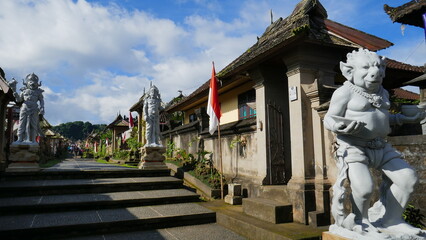 Hauptstraße durch das Museumsdorf Penglipuran in Bali mit traditionellen Häusern und großen Skulpturen © globetrotter1