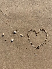 on the beach with Shells a heart symbol is carved into the smooth sand 