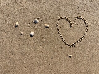 on the beach with Shells a heart symbol is carved into the smooth sand 