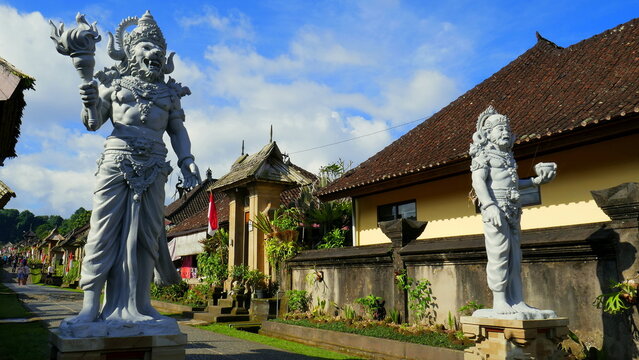 großen Skulpturen stehen entlang der Straße des  Dorfes Penglipuran in Bali mit traditionellen Häusern