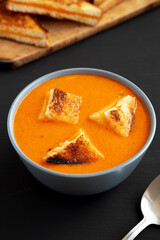 Homemade Tomato Soup with Grilled Cheese Croutons on a black background, side view.