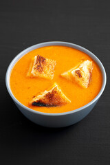 Homemade Tomato Soup with Grilled Cheese Croutons on a black surface, side view.