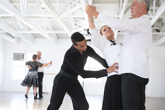 Mixed race dance teacher helping his ballroom dancing class