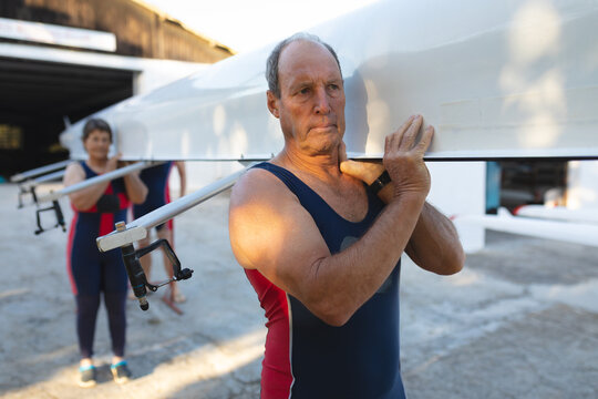 Senior caucasian rowing couple carrying boat on their shoulders to the lake - Powered by Adobe
