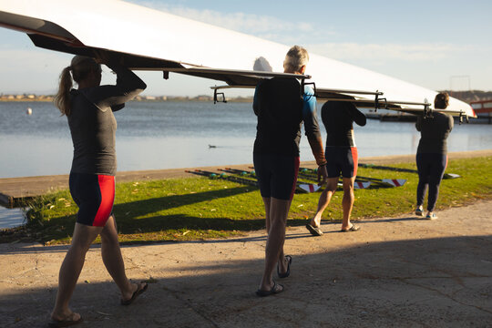 Rear view of senior caucasian rowing team carrying boat together to the lake