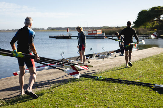 Senior caucasian rowing team carrying oars to the boat near the wooden dock