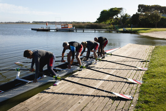 Senior caucasian rowing team attaching oars to the boat near the wooden dock