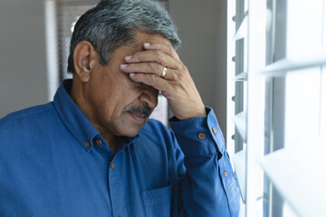 Senior mixed race man in kitchen holding his head in thought