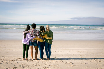 Group of diverse female friends embracing and standing on the beach