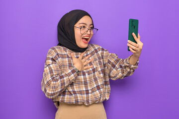 Shocked young Asian woman in plaid shirt using a mobile phone, getting great news isolated on purple background