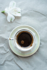 cup of coffee and white flower on gray background. top view