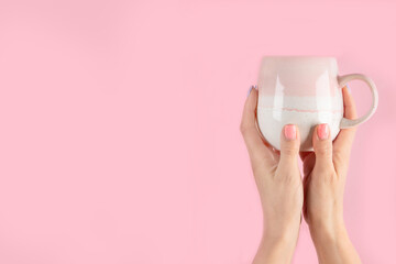 Arms raised up holding coffee cup on pink background.