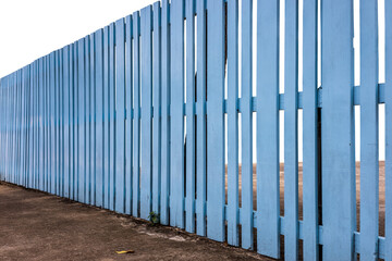 Isolate, side view, an old wooden fence painted in a beautiful blue color, which stretches over a concrete floor to surround a house.