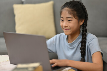 Happy Asian preteen girl school distance learning online at virtual class with teacher tutor on laptop by video conference call, watching online lesson at home.