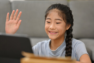 Happy cheerful Asian girl waving hand hello, talking on video call with her family or friends.