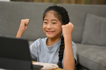 Asian little girl celebrating victory, feeling excited like winner when she playing game on tablet.