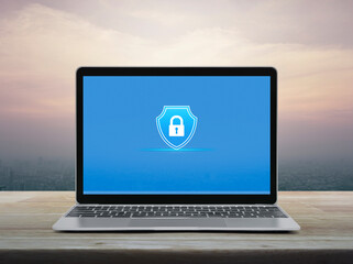 Padlock with shield flat icon on modern laptop computer monitor screen on wooden table over office city tower and skyscraper at sunset sky, vintage style, Technology security insurance online concept