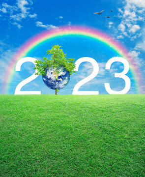 2023 white text with planet and tree on green grass field over rainbow, birds and blue sky, Happy new year 2023 ecological cover, Save the earth concept, Elements of this image furnished by NASA