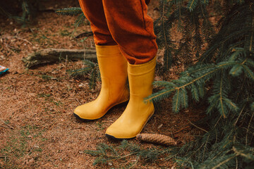Stylish female in yellow rubber boots stands near spruce tree