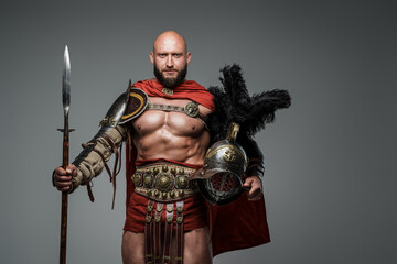Naklejka premium Shot of antique roman warrior with muscular build holding helmet and spear.