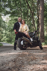 Fototapeta na wymiar Young beautiful couple hugging, sitting on a motorcycle, travel together on a forest road