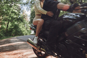 Fototapeta na wymiar Blurred Motion A young happy couple rides a motorcycle on an asphalt road in the forest, freedom and speed, in motion