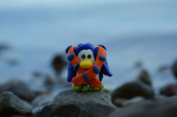 Obraz premium A toy penguin in a scarf on the background of the sea. Evening twilight. Beautiful toys.