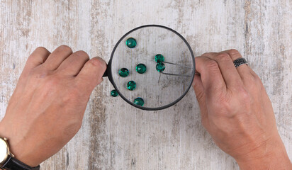 hand with a magnifying glass looks at the emerald