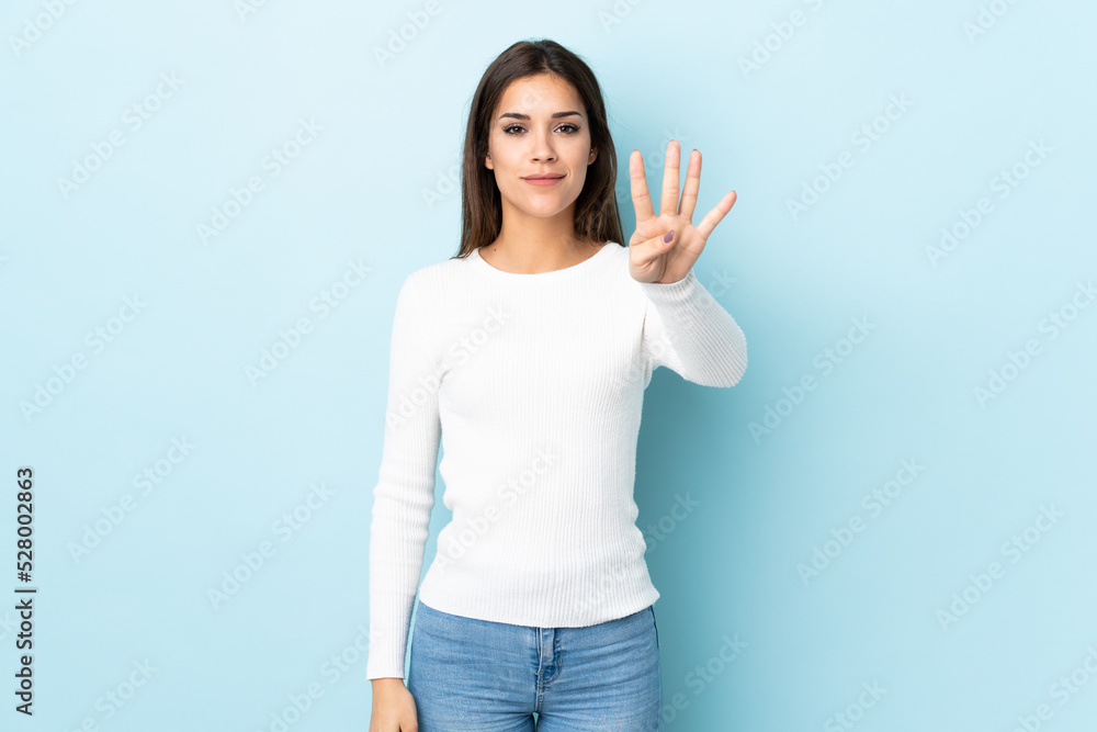 Wall mural Young caucasian woman isolated on blue background happy and counting four with fingers