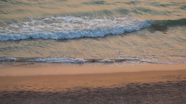 Handheld high angle shot of sea waves at Cabo De Rama Beach during the sunset as seen from a cliff besides the beach at South Goa in India. View of the sea waves during the sunset on a clean beach.