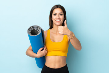 Young sport woman with mat isolated on blue background with thumbs up because something good has happened