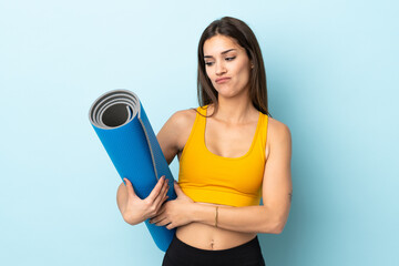 Young sport woman with mat isolated on blue background with sad expression
