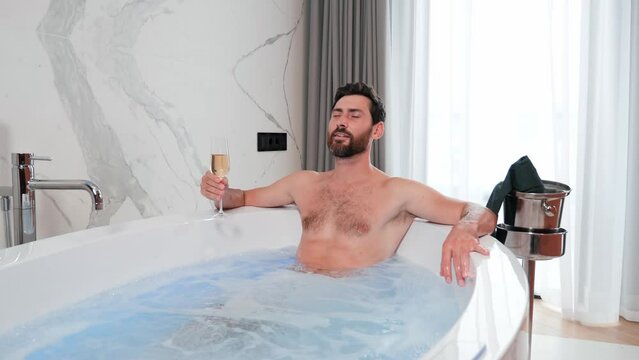 Close up of sexy businessman enjoying jacuzzi spa in hotel after well done job drinking champagne. Portrait of handsome guy relaxing in in the bath. Attractive man having hydro massage indoor. 