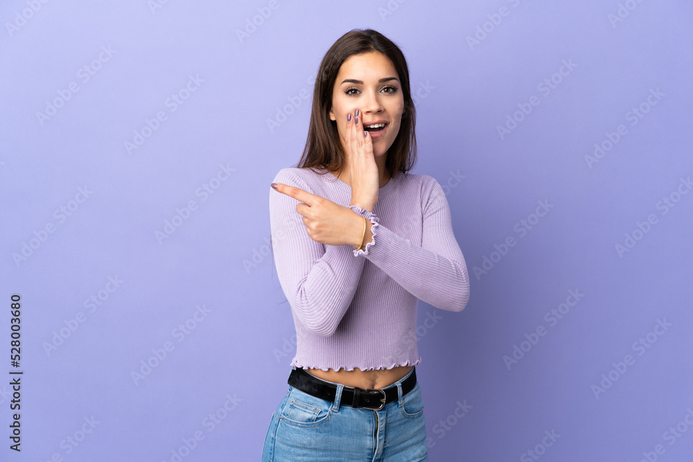 Poster Young caucasian woman over isolated background pointing to the side to present a product and whispering something