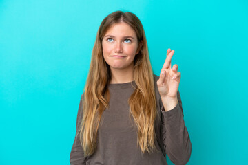 Young blonde woman isolated on blue background with fingers crossing and wishing the best